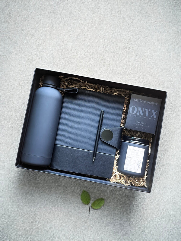 Gift set with stationery items including a notebook, pen, and bottle, coffee 'ONYX' on a light gray background.