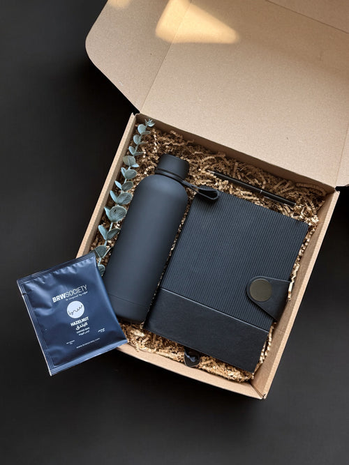 Set of black water bottle, notebook, and instant coffee in a gift box on a dark background