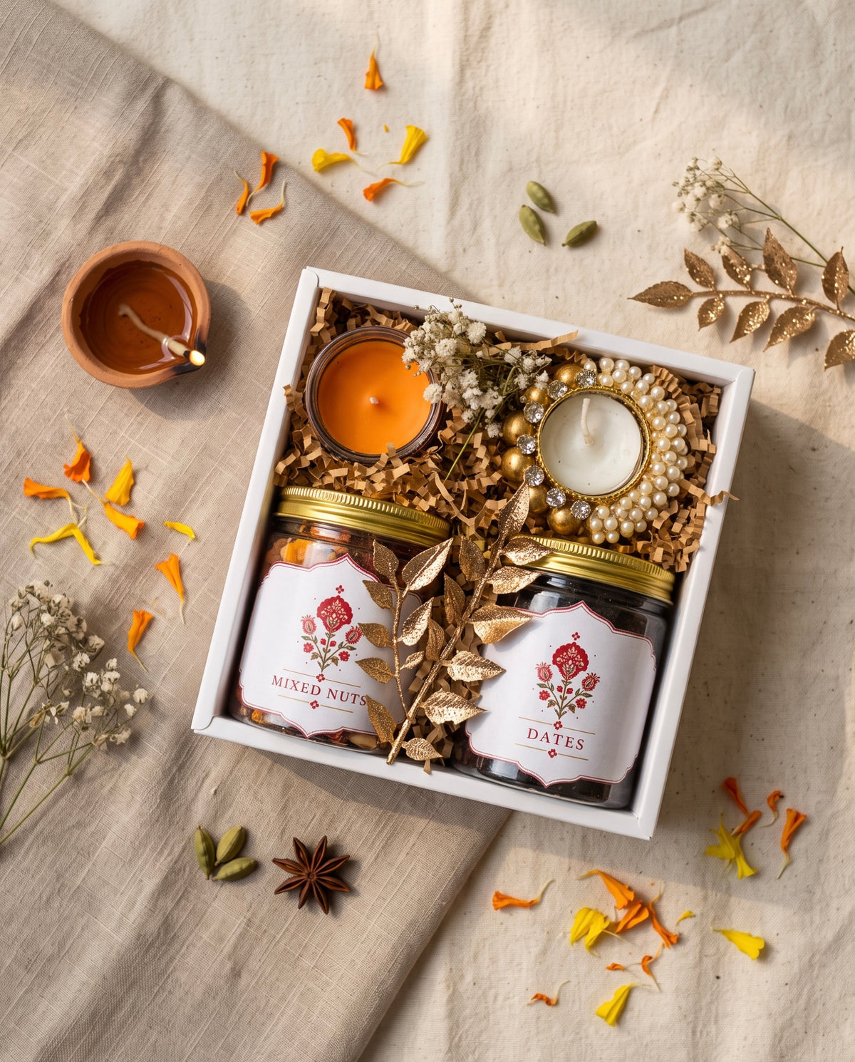 Mini Diwali Box with mixed nuts and dates, candle, and decorative elements on a soft fabric background.