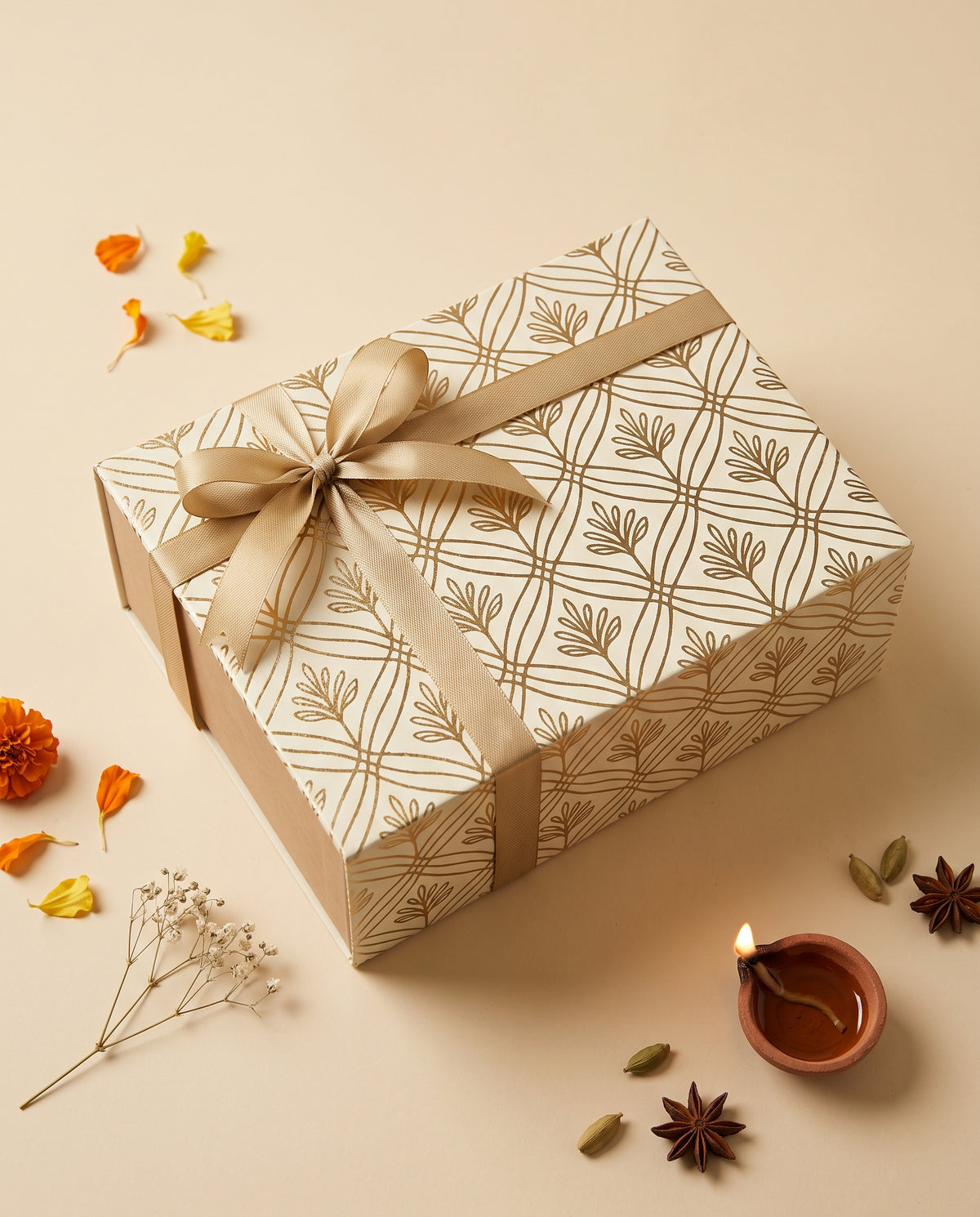 Earthy Glow Diwali Hamper wrapped in elegant gold-patterned paper with a ribbon, accompanied by festive decor.