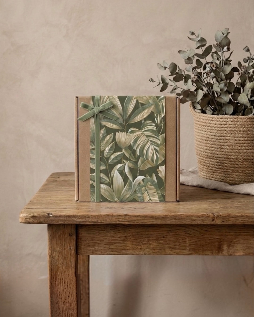 Nature-inspired wellness gift set packaging with green leaves, placed on a wooden table next to a potted plant.