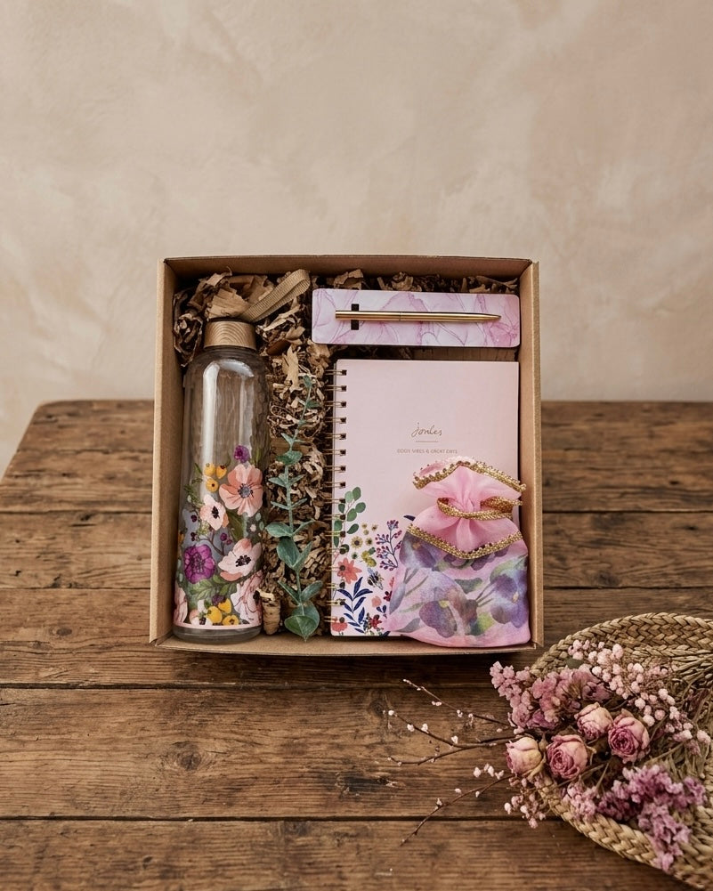 Botanical gift box for women featuring a floral glass bottle, spiral notebook, gold pen, and pink satin pouch.