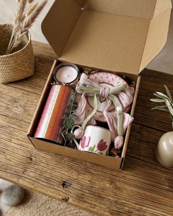 Open kraft box showcasing the tulip gift set with chocolates, a ceramic cup, saucer, candle, and hair clip.